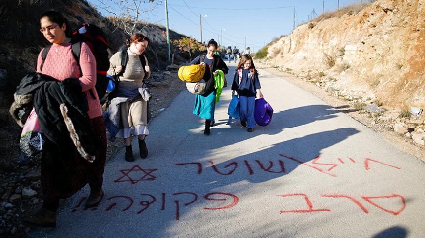 Israeli teenagers walk on graffiti reading in Hebrew "Soldier, policeman, refuse orders" as they prepare for an expected eviction of the Jewish settlement outpost of Amona in the West Bank, December 9, 2016. REUTERS/Amir Cohen TPX IMAGES OF THE DAY - RTSVF4Q