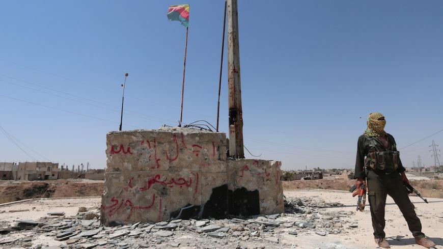 A Kurdish fighter stands with his weapons near a fluttering Kurdish flag in the Ghwairan neighborhood of Hasaka, Syria, August 23, 2016.REUTERS/Rodi Said - RTX2MP4F