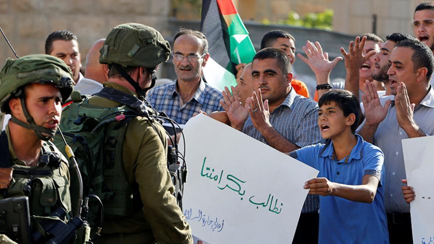 A Palestinian boy holds a sign that reads "we demand our dignity" in front of Israeli soldiers during a protest calling for the reopening of a closed street in the West Bank city of Hebron August 24, 2016. REUTERS/Mussa Qawasma - RTX2MW1E