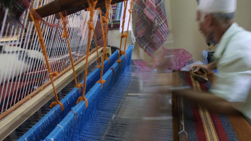 Palestinian Ibrahim al-shobaky, 50, works on weaving a carpet at an arts and crafts village in Gaza City 13 July 2003. Craftsmen at the center, established by the Gaza City municipality in the mid-1990s, use an authentic loom to produce their colorful rugs, bags, cushion covers and bedspreads. A variety of other woolen products are produced at the center from, sheep, goat and camel wool, all dyed by hand the traditional way.  AFP PHOTO/MAHMOUD HAMS  (Photo credit should read MAHMUD HAMS/AFP/Getty Images)