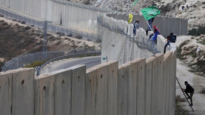 Palestinian protesters climb over a section of the Israeli barrier that separates the West Bank town of Abu Dis from Jerusalem, during an anti-Israel protest, November 16, 2015. REUTERS/Ammar Awad   - RTS7CY7
