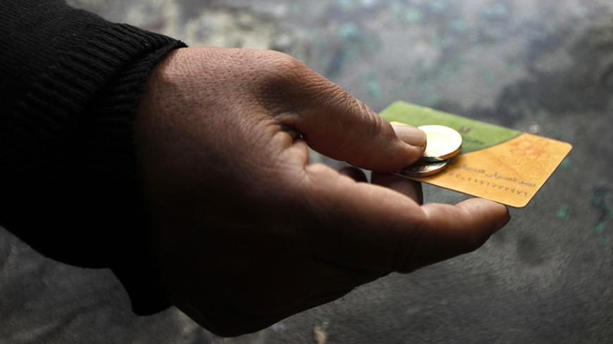 A man holds his smart card and some coins at a bakery in the Suez Canal city of Port Said, 170 km (106 miles) northeast of Cairo, February 24, 2014. A device resembling a credit card swiper is revolutionizing some of Egypt's politically explosive bread lines and may help achieve the impossible -- cutting crippling food import bills. Authorities who hope to avoid protests over subsidised loaves sold for the equivalent of one U.S. cent have turned to smart cards to try to manage the corrupt and wasteful bread