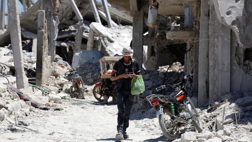 A man walks while using his phone past damaged buildings in Deraa, Syria July 15, 2017. REUTERS/Alaa Al-Faqir - RTX3BL5E