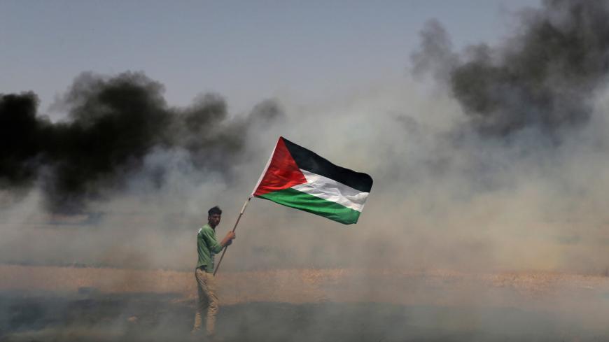 A demonstrator holds a Palestinian flag during clashes with Israeli troops at a protest where Palestinians demand the right to return to their homeland, at the Israel-Gaza border in the southern Gaza Strip, April 13, 2018. REUTERS/Ibraheem Abu Mustafa TPX IMAGES OF THE DAY - RC151862B9A0