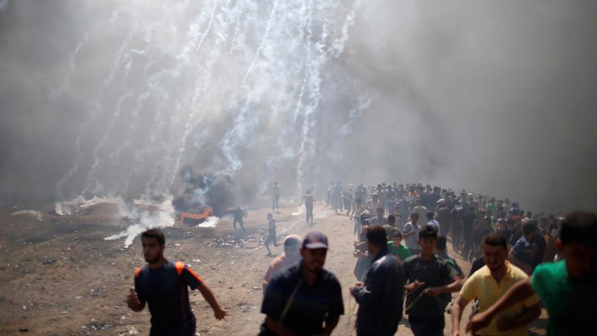Palestinian demonstrators run from tear gas fired by Israeli troops during a protest against U.S. embassy move to Jerusalem and ahead of the 70th anniversary of Nakba, at the Israel-Gaza border east of Gaza City May 14, 2018. REUTERS/Mohammed Salem TPX IMAGES OF THE DAY - RC1385445700