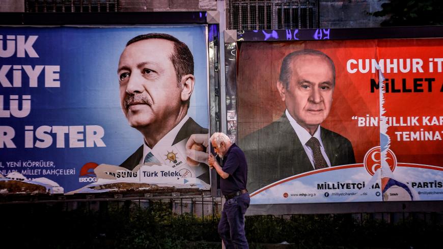 A pedestrian lights a cigarette as he walks past in banners with portraits of Turrkish President Recep Tayyip Erdogan (L) and the leader of Nationalist Movement Party (MHP) Devlet Bahceli in Istanbul on June 19, 2018. - Turkey is preparing for tight presidential and parliamentary elections on June 24, while many analysts say President Erdogan wants a major foreign policy success to give him a final boost. (Photo by Aris MESSINIS / AFP) (Photo credit should read ARIS MESSINIS/AFP/Getty Images)