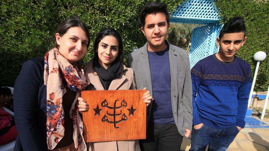 A woman poses in a group photo with a wooden cut-out depicting the ringstone symbol of the Baha'i faith during a carnival commemorating International Minority Rights Day in the southern Iraqi city of Basra on December 16, 2017. (Photo by HAIDAR MOHAMMED ALI / AFP)        (Photo credit should read HAIDAR MOHAMMED ALI/AFP/Getty Images)