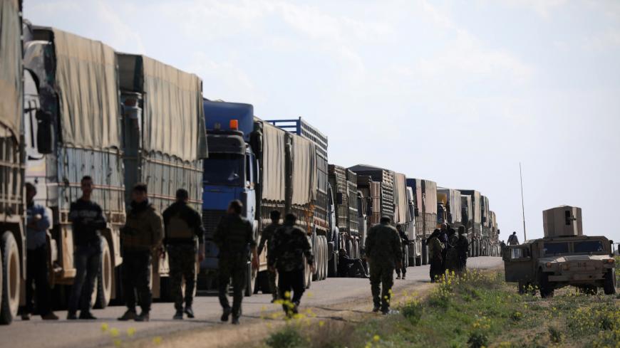 Fighters from Syrian Democratic Forces (SDF) walk near a convoy of trucks near the village of Baghouz, Deir Al Zor province, Syria February 20, 2019. REUTERS/Rodi Said - RC19B5E17C00