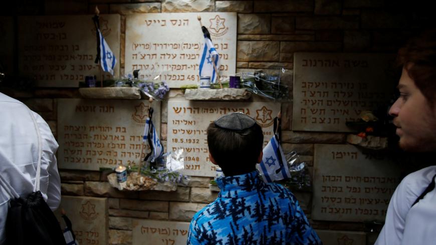 A youth looks at flowers and flags laid next to tombstones on Memorial Day, when Israel commemorates it's fallen soldiers, at Mount Herzl military cemetery in Jerusalem May 8, 2019. REUTERS/Ronen Zvulun - RC1C955B89F0