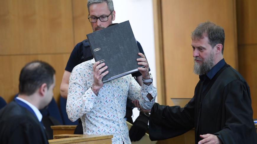 Defence lawyers Serkan Alkan (L) and Martin Heising (R) look on as the Iraqi defendant, identified only as Taha al-J., believed to have belonged to the Islamic State (IS) jihadist group, hides his face while arriving into the courtroom for the start of his trial for genocide and murdering a young Yazidi girl, he held as a slave, on April 24, 2020 at the Higher Regional Court (OLG) in Frankfurt am Main. - Defence lawyers Serkan Alkan (L) and Martin Heising (R) look on as the Iraqi defendant, identified only