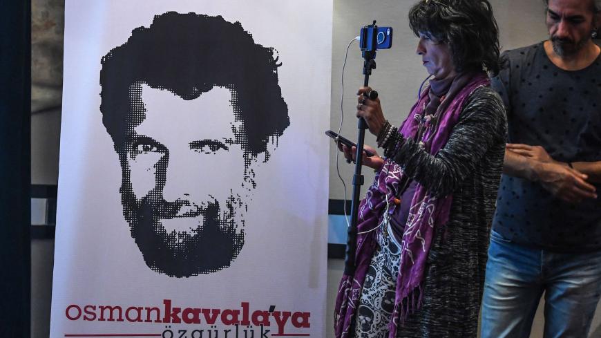 A journalist stands in front of a poster featuring jailed businessman and philanthropist Osman Kavala during a press conference of his lawyers on October 31, 2018. - Osman Kavala was arrested a year ago by Turkish authorities and has still to be charged with an offence. (Photo by OZAN KOSE / AFP) (Photo credit should read OZAN KOSE/AFP via Getty Images)