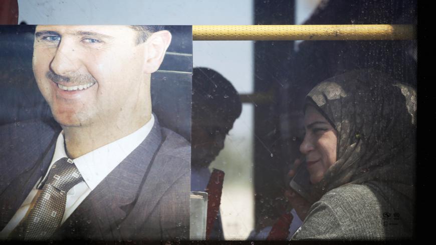 A returnee sits in a bus next to a picture of Syrian President Bashar al Assad in Qusayr, Syria July 7, 2019. REUTERS/Omar Sanadiki - RC16FEE06D50