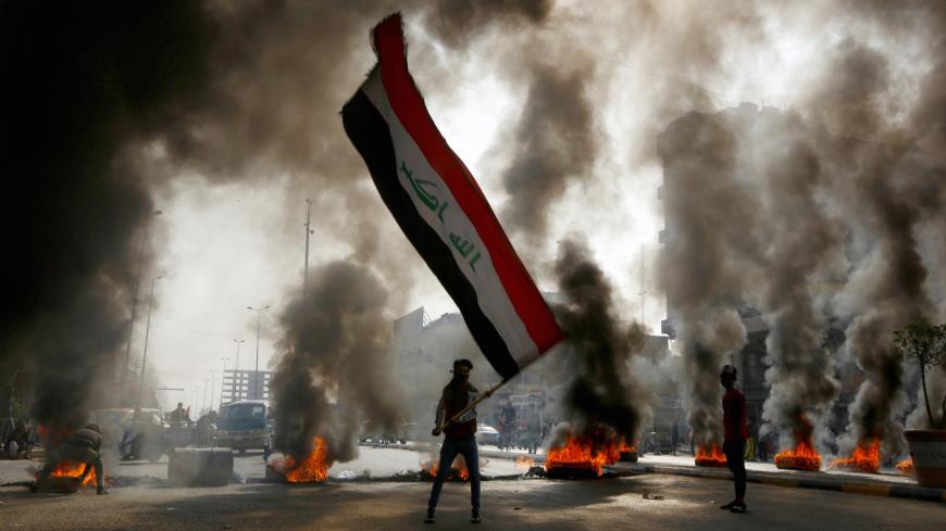 A protester holds an Iraqi flag amid a cloud of smoke from burning tires during ongoing anti-government protests in Najaf, Iraq November 26, 2019. REUTERS/Alaa al-Marjani - RC2ZID9MARY6