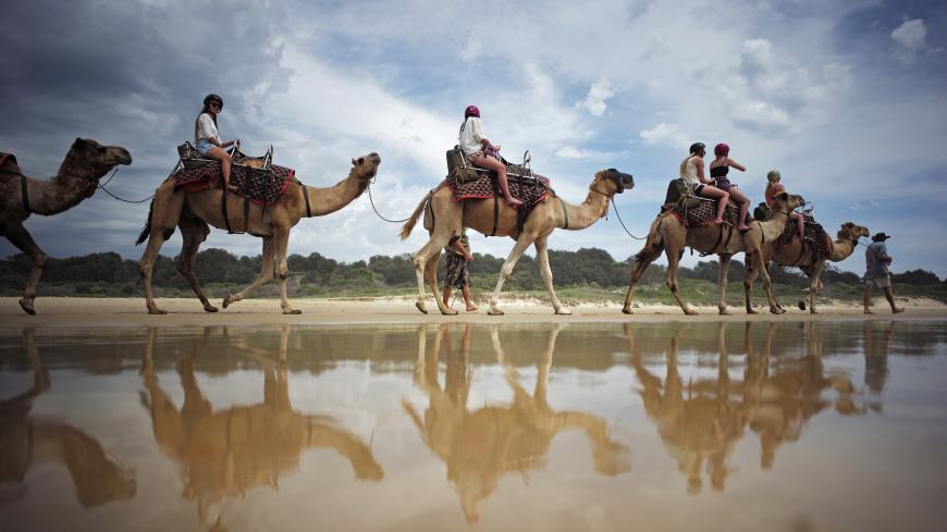 Tourists are reflected in the waters of the Pacific Ocean as they ride on a camel safari along Lighthouse Beach, north of Sydney, December 4, 2014. For 25 years camel rides on this beach have given visitors to Australia's holiday coast a rare experience available only in a handful of locations in the country. Australia's long history with the 'ships of the desert' goes back to the 1800s when they were imported from Afghanistan and India for use as transportation across Australia's vast deserts before being
