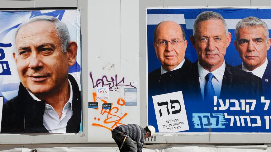 A labourer walks past electoral campaign posters bearing the portraits of Israel's Prime Minister Benjamin Netanyahu (L), leader of the Likud party, and retired Israeli general Benny Gantz (R), one of the leaders of the Blue and White (Kahol Lavan) political alliance, in the Israeli city of Tel Aviv, on April 3, 2019, ahead of the general election scheduled for April 9. (Photo by JACK GUEZ / AFP) (Photo credit should read JACK GUEZ/AFP via Getty Images)