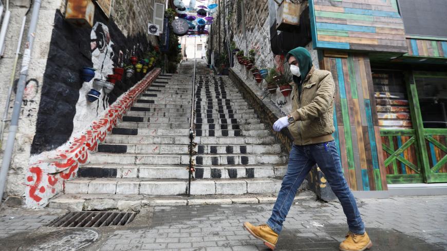 A man wearing a protective face mask walks next to closed shops as the country takes measures to fight the spread of the coronavirus disease (COVID-19), in Amman, Jordan, March 18, 2020. REUTERS/Muhammad Hamed - RC2FMF95PIXF