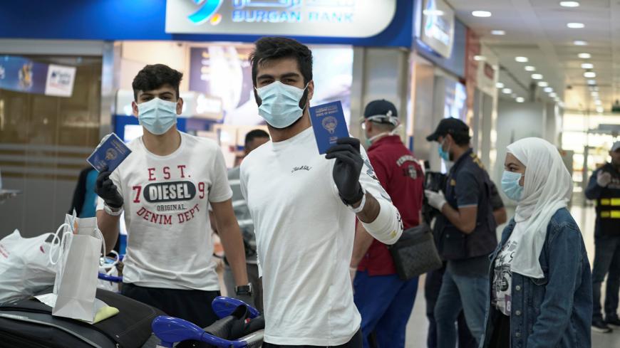 Kuwaiti boys wearing protective face masks and quarantine tracking bracelets, following the outbreak of the coronavirus disease (COVID-19), pose for the camera as they hold up their passports upon arrival from Amman, to Kuwait Airport in Kuwait, Kuwait April 21, 2020. REUTERS/Stephanie McGehee - RC229G91CPDO