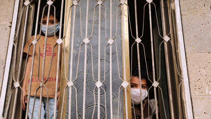 Children wearing protective masks look from behind a window during a 24-hour curfew amid concerns about the spread of the coronavirus disease (COVID-19), in Sanaa, Yemen May 6, 2020. REUTERS/Khaled Abdullah - RC25JG9G88PF