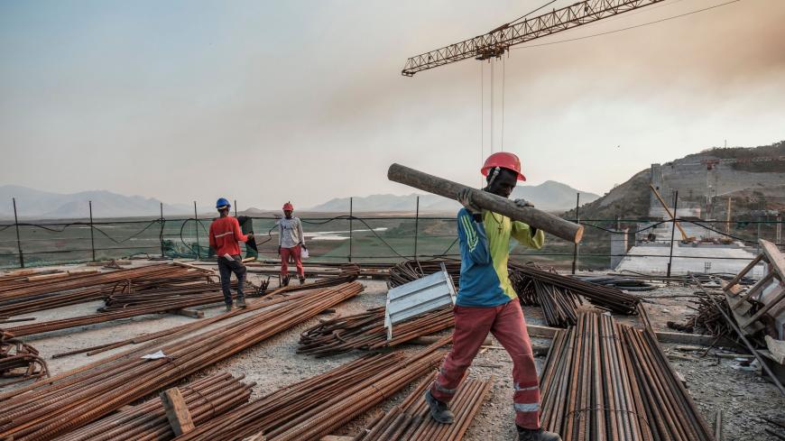 A worker walks with a piece of wood on his shoulder at the Grand Ethiopian Renaissance Dam (GERD),  near Guba in Ethiopia, on December 26, 2019. - The Grand Ethiopian Renaissance Dam, a 145-metre-high, 1.8-kilometre-long concrete colossus is set to become the largest hydropower plant in Africa.
Across Ethiopia, poor farmers and rich businessmen alike eagerly await the more than 6,000 megawatts of electricity officials say it will ultimately provide. 
Yet as thousands of workers toil day and night to finish 