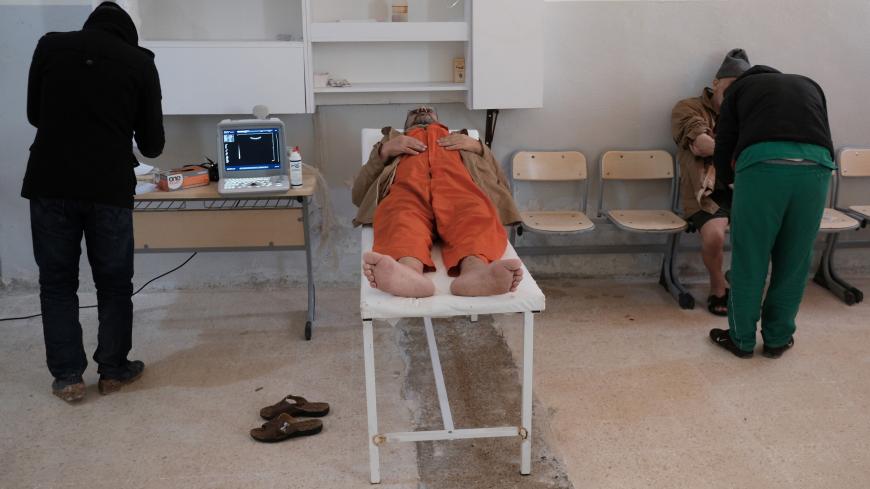 A foreign prisoner, suspected of being part of the Islamic State, lies on top of an examining table next to a doctor inside a prison in Hasaka, Syria, January 7, 2020.  REUTERS/Goran Tomasevic      SEARCH "ISLAMIC STATE PRISONERS" FOR THIS STORY. SEARCH "WIDER IMAGE" FOR ALL STORIES. - RC2YYE9HG8VE