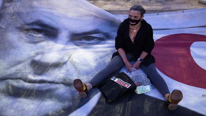 TEL AVIV, ISRAEL - APRIL 19: A woman sits on a placard showing Israeli Prime Minister Benjamin Netanyahu, as she protests at a rally in Rabin Square on April 19, 2020 in Tel Aviv, Israel. Thousands of Israelis gather at an Anti-Corruption rally under coronavirus restrictions, decrying proposed unity government talks between Israeli Prime Minister Benjamin Netanyahu, and Blue and White Party leader Benny Gantz. (Photo by Amir Levy/Getty Images)