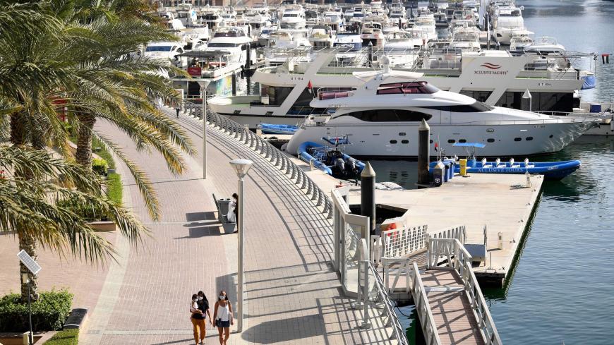 Women wearing protective masks walk at the promenade of Dubai Marina on May 5, 2020, after authorities of the United Arab Emirates started to ease a national lockdown put in place to curb the spread of COVID-19 coronavirus. - In Dubai's ritzy Marina district, white yachts are tethered to docks, standing idle -- like many companies behind a luxury lifestyle industry battered by the coronavirus crisis. The boardwalks that snake around the precinct's artificial bays and canals, once packed with tourists, mostl