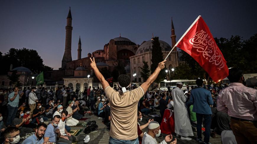 A man flashes the V for Victory hand sign and waves a flag outside the Hagia Sophia museum in Istanbul on July 10, 2020 as people gather to celebrate after a top Turkish court revoked the sixth-century Hagia Sophia's status as a museum, clearing the way for it to be turned back into a mosque. - The Council of State, the country's highest administrative court which on July 2 debated a case brought by a Turkish NGO, cancelled a 1934 cabinet decision and ruled the UNESCO World Heritage site would be reopened t