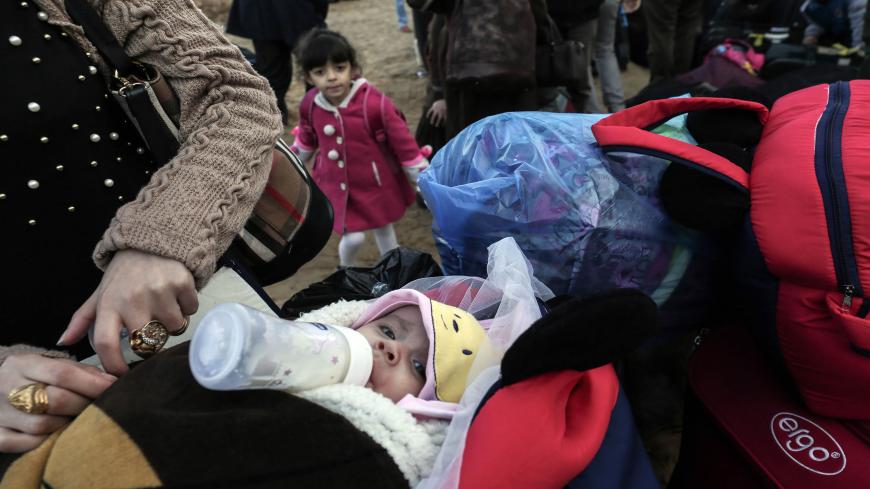 A picture taken on December 16, 2017 shows a woman standing by an infant with a milk bottle in their mouth as they wait to ride a bus in Khan Younis in the southern Gaza strip, prior to departure for the Rafah border crossing with Egypt. / AFP PHOTO / SAID KHATIB        (Photo credit should read SAID KHATIB/AFP via Getty Images)
