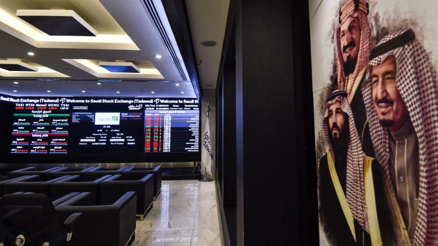 This picture taken December 12, 2019 shows (L) a view of the exchange board at the Stock Exchange Market (Tadawul) bourse in Riyadh displaying Aramco shares on the second day of their trading, along with a poster depicting Saudi Arabia's founder King Abdulaziz ibn Saud (C), his son and current King Salman bin Abdulaziz (R), and the latter's son Crown Prince Mohammed bin Salman (L) on display. - Energy giant Saudi Aramco's market value soared above $2 trillion as its share price surged again on its second da