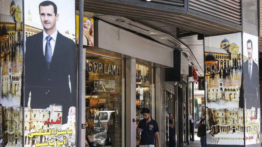 A man walks past window shops while nearby pillars are adorned with posters showing Syrian PResident Bashar al-Assad superimposed over Damascus' historic Umayyad mosque, in al-Salihiya district of the capital Damascus on June 10, 2020. (Photo by LOUAI BESHARA / AFP) (Photo by LOUAI BESHARA/AFP via Getty Images)