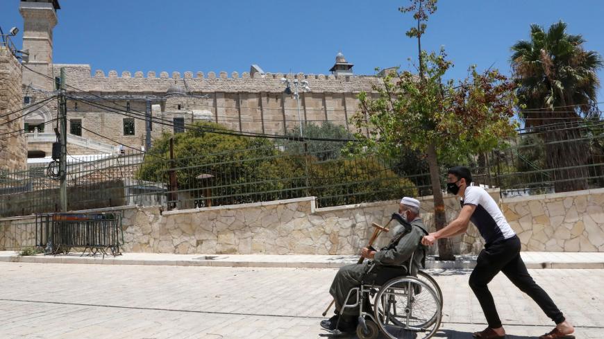 A Palestinian youth pushes an elderly man next to the Ibrahimi mosque (background), also known as the Tomb of the Patriarchs, in the occupied West Bank city of Hebron on August 7, 2020, amid the ongoing coronavirus pandemic crisis. (Photo by HAZEM BADER / AFP) (Photo by HAZEM BADER/AFP via Getty Images)
