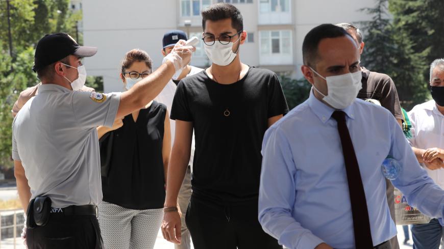 A man takes the temperature of worshippers ahead of the Friday prayer at Kocatepe Mosque on August 7, 2020, amid the crisis linked with the Covid-19 pandemic caused by the novel coronavirus. (Photo by Adem ALTAN / AFP) (Photo by ADEM ALTAN/AFP via Getty Images)