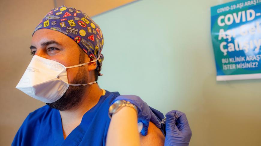 A health worker administers a dose of Sinovac Biotech potential vaccine against the COVID-19 to Doctor Cem Gun (L) during the 3rd phase trials at the Acibadem Hospital in Istanbul, on October 9, 2020.Y (Photo by Yasin AKGUL / AFP) (Photo by YASIN AKGUL/AFP via Getty Images)