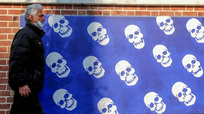 An Iranian man wearing a protective mask amid the COVID-19 pandemic, walks past a mural painted on the outer walls of the former US embassy in the capital Tehran, on December 30, 2020. (Photo by ATTA KENARE / AFP) (Photo by ATTA KENARE/AFP via Getty Images)