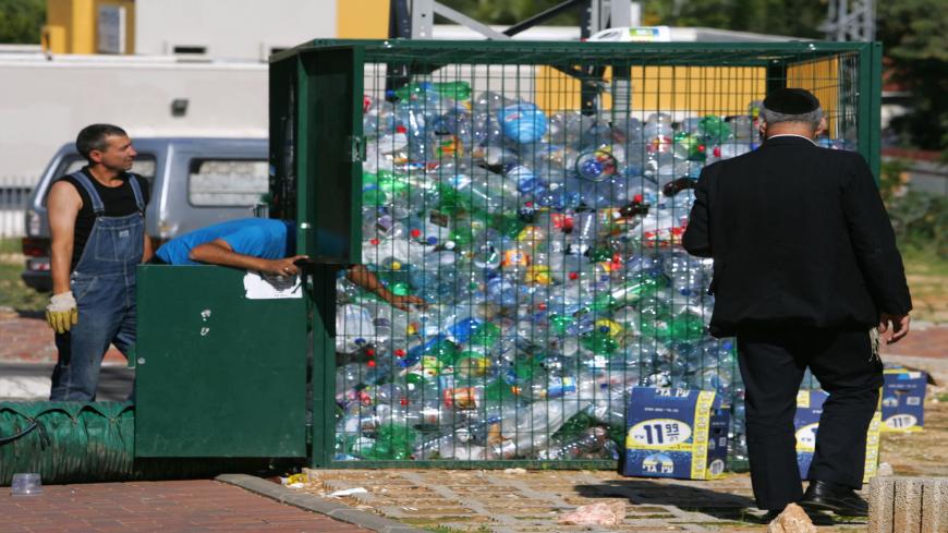 ROSH HA'AYIN, ISRAEL - NOVEMBER 21: A passing ultra-Orthodox Jew watches as Aviv Recycling workers use a strong vacuum to move plastic bottles from a collection cage into their truck November 21, 2006 in Rosh Ha'Ayin in central Israel. Aviv managers say they recycle about 15 percent of the country's PET plastic waste annually, some 4,000 metric tons or 80 million bottles, but have the capacity to sort, clean, crush and sell more than double that if recycling programs in Israel were more efficient.  (Photo b