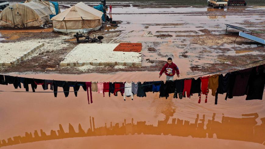 TOPSHOT - A boy walks through a rainwater pond near a laundry line with clothes hanging out to dry at a flooded camp for Syrians displaced by conflict near the village of Kafr Uruq, in Syria's northern rebel-held Idlib province on January 17, 2021. (Photo by OMAR HAJ KADOUR / AFP) (Photo by OMAR HAJ KADOUR/AFP via Getty Images)