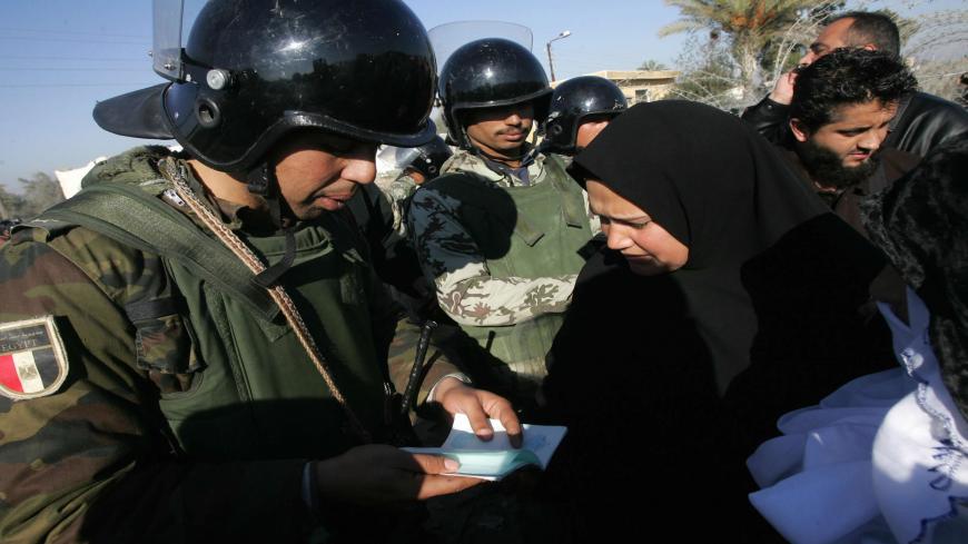 An Egyptian security officer checks the travel document of a Palestinian woman returning home through the one gate that remained open in the newly erected border fence between Egypt and the southern Gaza Strip town of Rafah, 03 February 2008. Egyptian and Hamas forces sealed off the border between Gaza and Egypt today after reportedly agreeing to control the frontier, blown open nearly two weeks ago amid an Israeli blockade. AFP PHOTO/MAHMUD HAMS (Photo credit should read MAHMUD HAMS/AFP via Getty Images)