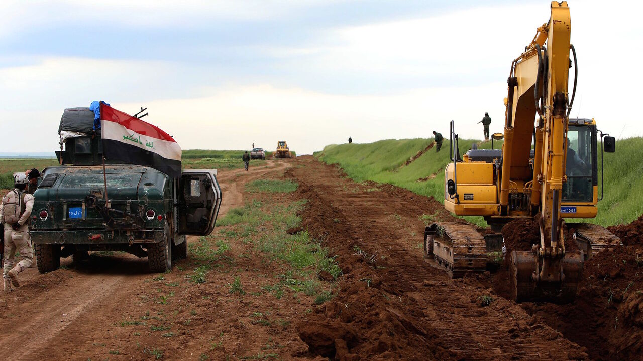 Iraqi security forces stand guard as workers are digging a trench on the northern Iraqi border with Syria to prevent people from crossing over into Iraq's autonomous Kurdistan region, on April 13, 2014 in Zakho. 