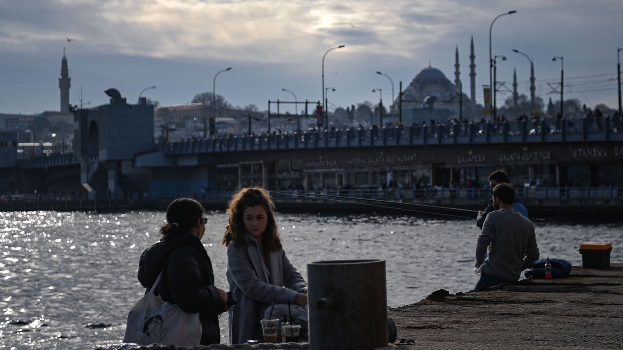 People sit along the Bosphorus shore at Karakoy port in Istanbul on Feb. 8, 2021 as the Galata bridge and the Suleymaniye mosque are seen in the background.