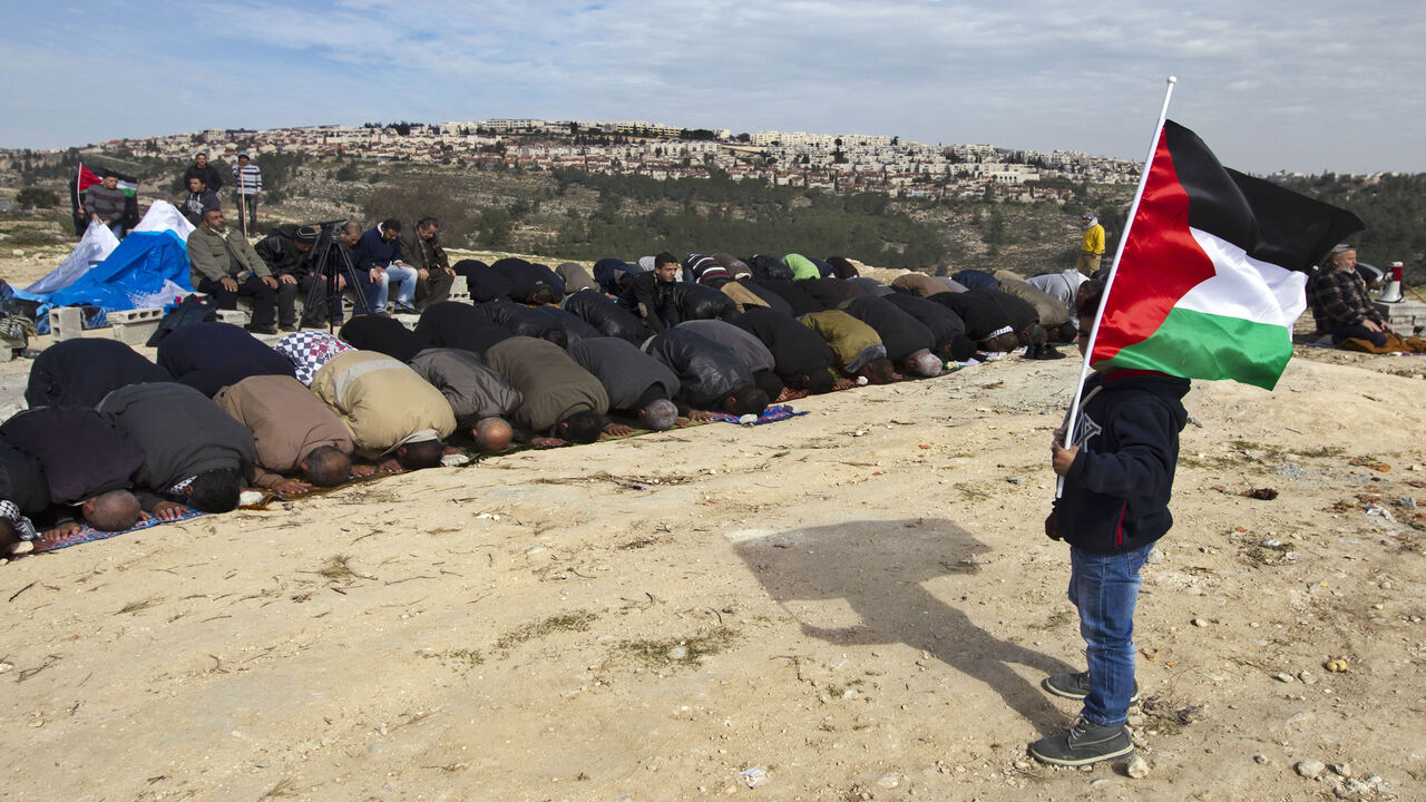 A young boy holds a flag as people pray during a protest of Palestinian activists over confiscated lands by the Israeli army in Beit Iksa, West Bank, Jan. 25, 2013.