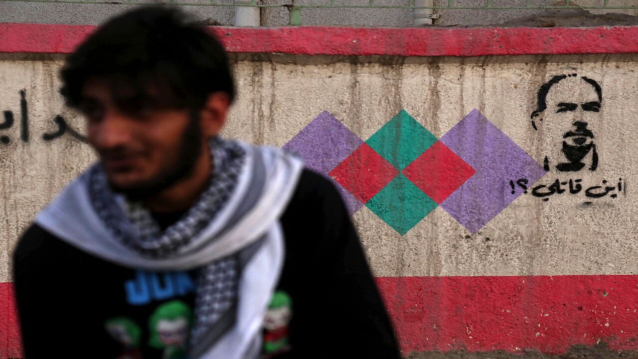 n Iraqi sits across graffiti reading in Arabic "Where's my killer?" and depicting renowned Iraqi anti-government activist Ihab al-Wazni (Ehab al-Ouazni), who was shot dead in an ambush earlier this month, in the shrine city of Karbala on May 23, 2021. A wave of deadly attacks on pro-democracy activists and journalists in Iraq has sparked mounting calls to boycott October parliamentary elections, as perpetrators go unpunished. Killings, attempted murder and abductions have targeted more than 70 activists sin