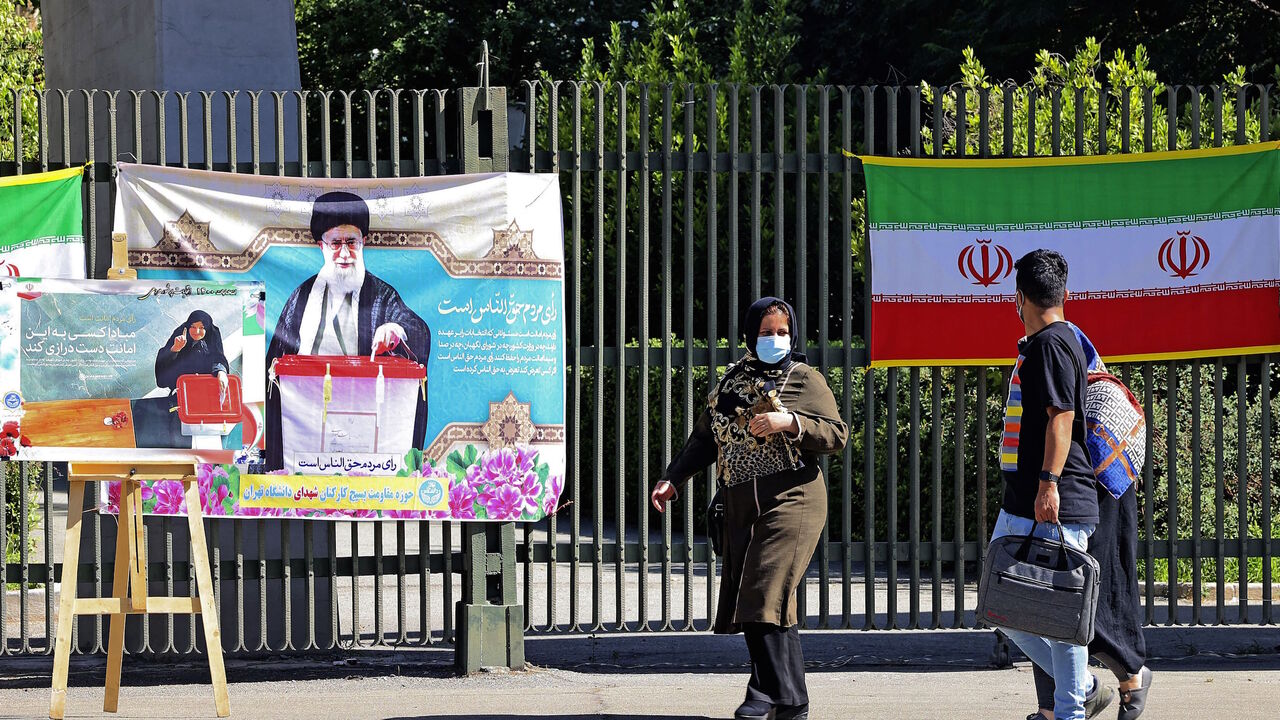 Iranians walk past banners encouraging people to vote hung on a fence at Tehran university in the eponymous capital, on June 14, 2021, ahead of the June 18 presidential elections. 