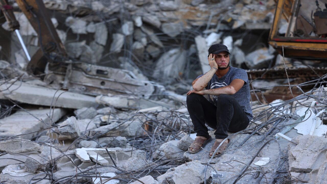 A Palestinian man sits on the rubble of a building destroyed by Israeli airstrikes last month in Gaza City on June 15, 2021.