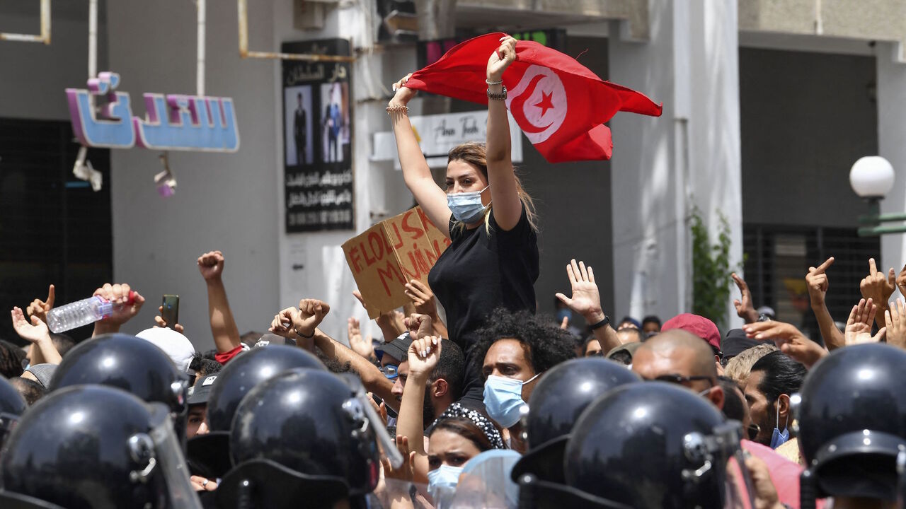 A Tunisian protester lifts a national flag at an anti-government rally as security forces block off the road in front of the Parliament in the capital Tunis on July 25, 2021.