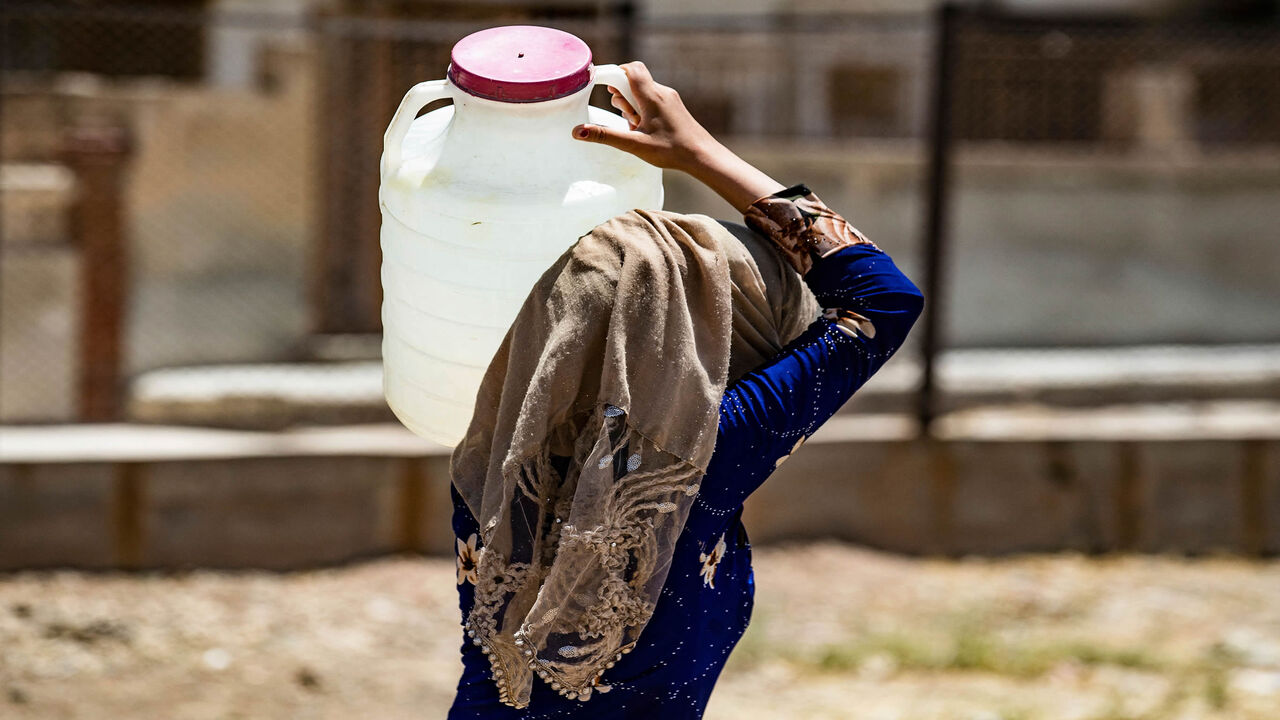 A Syrian woman carries a container of water provided by UNICEF in the northeastern city of Hasakah, after disruption in water supply from the Alouk station, Syria, July 8, 2021.