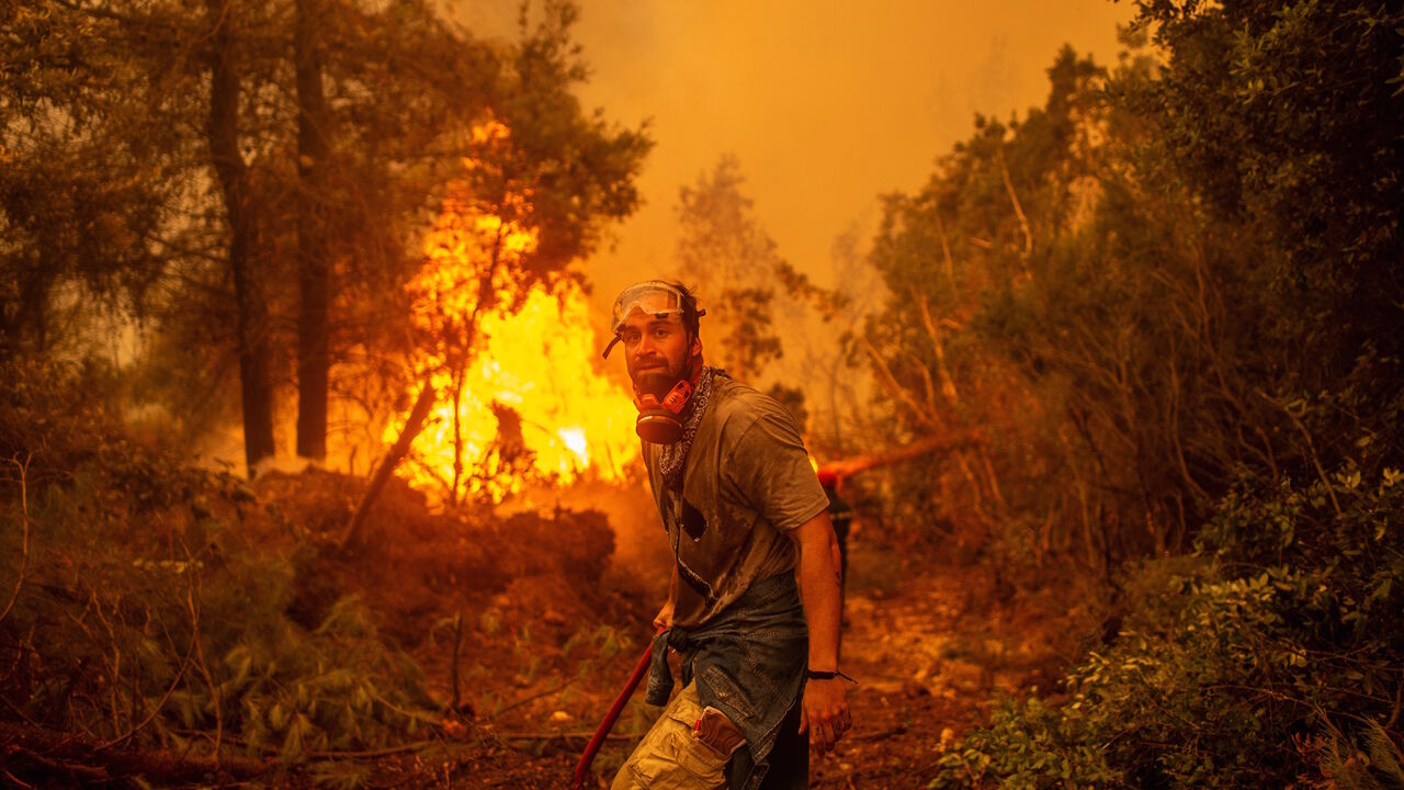 A volunteers holds a water hose near a burning blaze as he tries to extinguish a fire in the village of Glatsona on Evia (Euboea) island, on Aug. 9, 2021. 