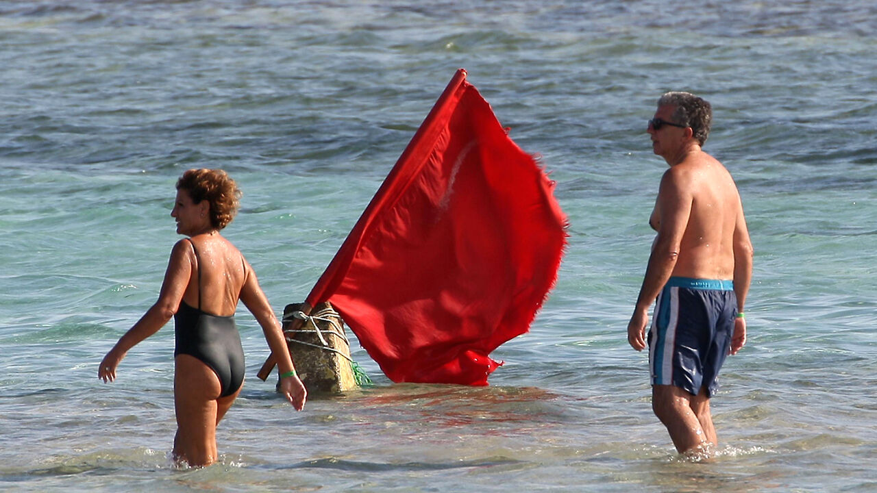 Tourists walk past a red flag serving as a warning of shark sightings on a beach in the Red Sea resort of Sharm el-Sheikh on Dec. 8, 2010. 