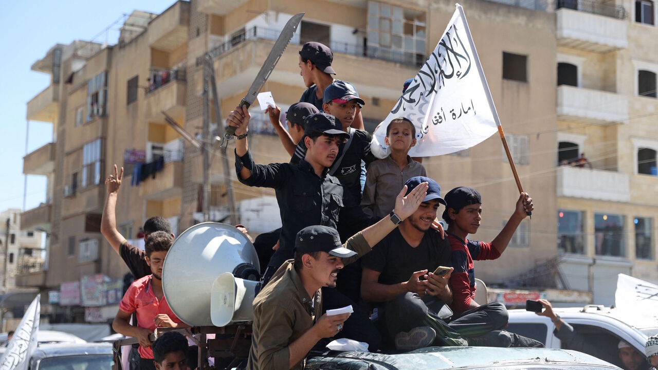 Members of Syria's top jihadist group the Hayat Tahrir al-Sham (HTS) alliance, led by al-Qaeda's former Syria affiliate, parade with their flags and those of the Taliban's declared "Islamic Emirate of Afghanistan" through the rebel-held northwestern city of Idlib on Aug. 20, 2021.