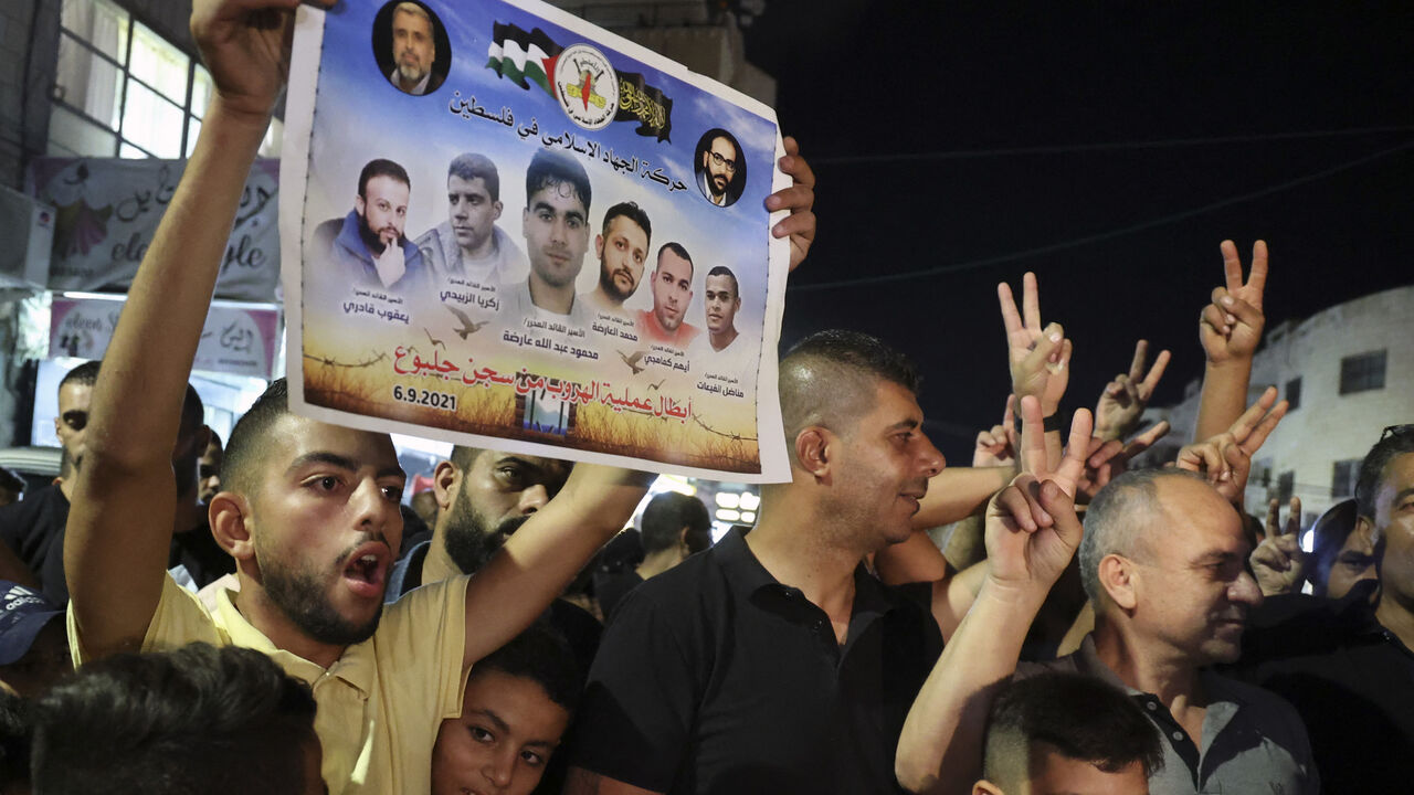 A Palestinian man flashes a poster by the militant group Islamic Jihad of the six Palestinians who escaped from an Israeli prison, as people celebrate in the Jenin camp in the northern Israeli-occupied West Bank, on Sept. 6, 2021.