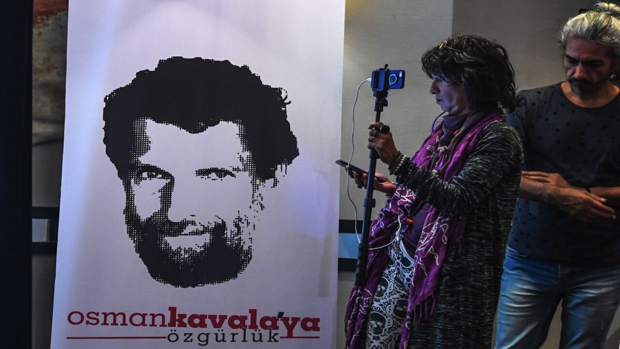 A journalist stands in front of a poster featuring jailed businessman and philanthropist Osman Kavala.